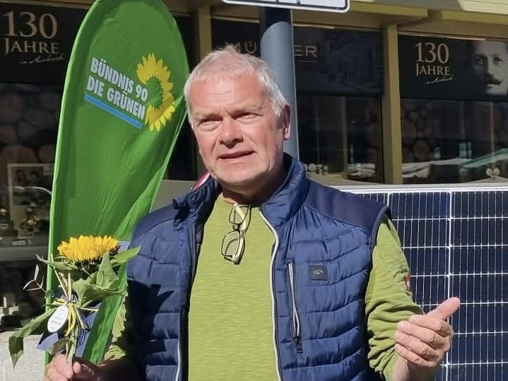 Solarexperte Martin Brugger vor einem Solarpanel mit Sonnenblume in der Hand